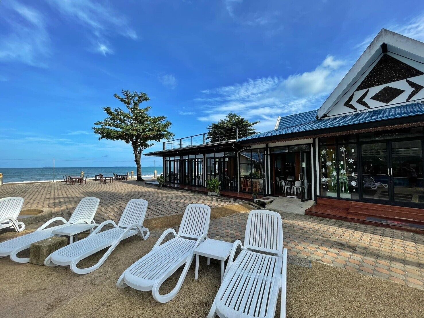 A beachfront property with white lounge chairs, a covered seating area, and a view of the ocean.