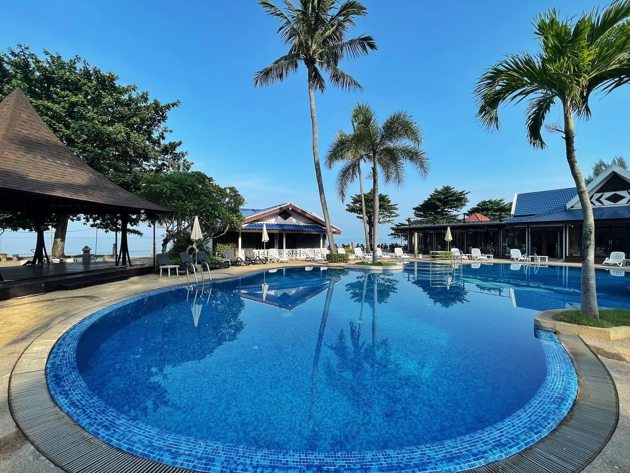 A pool with lounge chairs and palm trees, surrounded by buildings with a tropical theme.