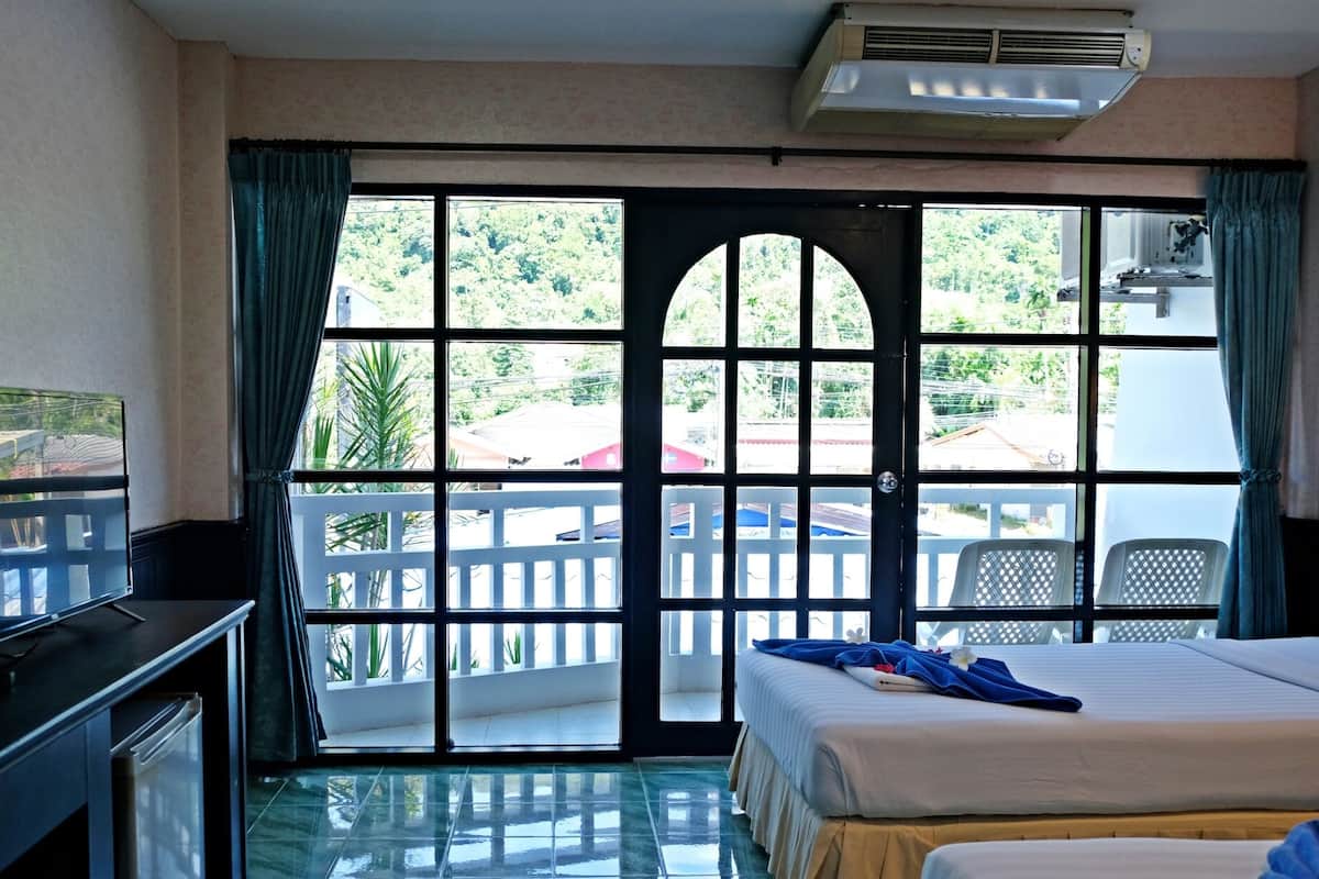 Quarto de hotel com cama, televisão, secretária e varanda com vista para o exterior.