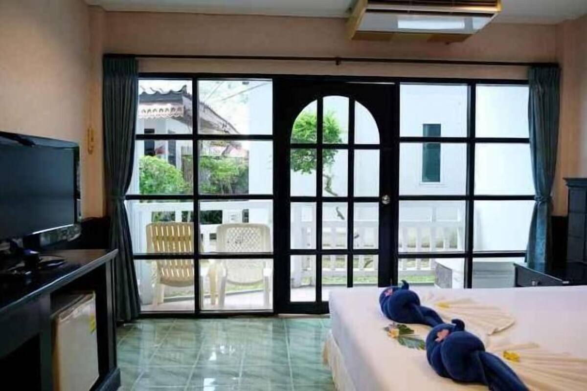 Quarto de hotel com uma cama, televisão e vista do exterior através de grandes janelas.