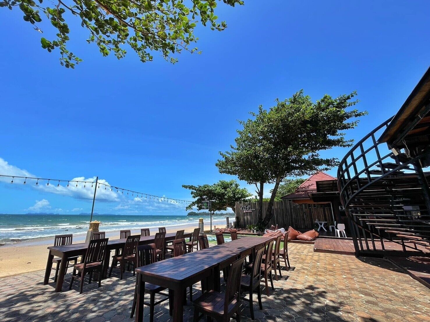 An outdoor seating area with wooden tables and chairs, overlooking a beach and ocean.