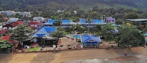 Un complejo turístico frente al mar con acceso a la playa, piscina y vistas a una colina boscosa.