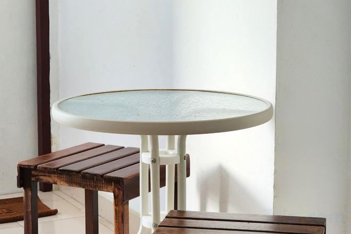 Una mesa redonda con superficie de vidrio y un taburete de madera a un lado.