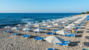 Μια παραλία με σειρές από μπλε ξαπλώστρες και λευκές ομπρέλες.