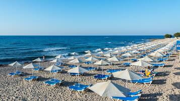 Een strand met rijen blauwe ligbedden en witte parasols.