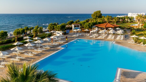 Ένας χώρος πισίνας σε ένα θέρετρο, με ξαπλώστρες και ομπρέλες, ένα μικρό κτίριο και θέα στη θάλασσα.