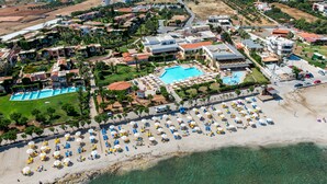Μια αεροφωτογραφία ενός θέρετρου με πολλές πισίνες, μια παραλία με ομπρέλες και μια ποικιλία κτιρίων.