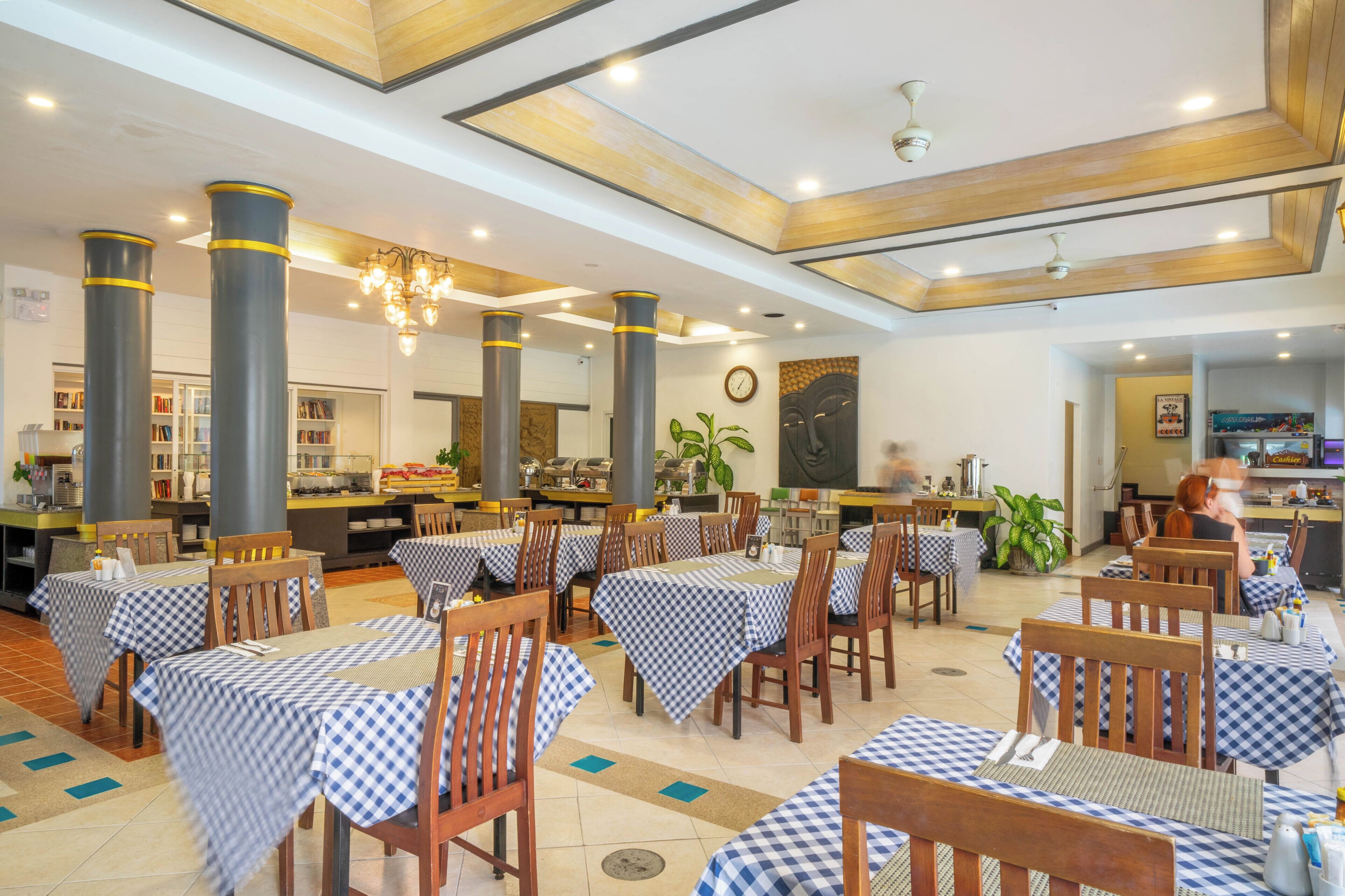 A spacious restaurant with checkered tablecloths, wooden chairs, and a central serving area.