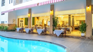 A poolside restaurant with outdoor seating, a pool, and a building with a balcony. - La Vintage Resort (Patong)