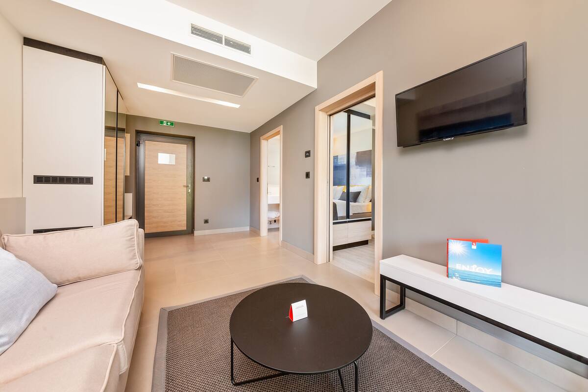 A modern hotel lobby with a sofa, a small table, a TV, and a bench.