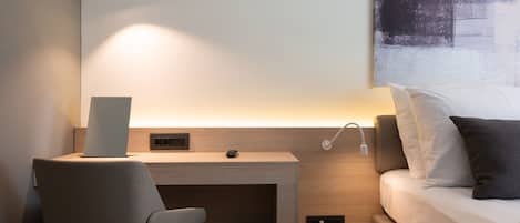 A modern hotel room with a desk, chair, and a bed.