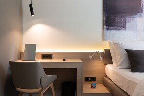 Moderni hotellihuone, jossa on työpöytä, tuoli ja sänky.