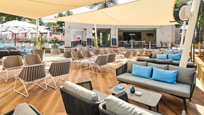 An outdoor seating area with various chairs and sofas, a pool in the background, and a covered section with tables and chairs. - Garden Suites Park Plava Laguna (Porec)