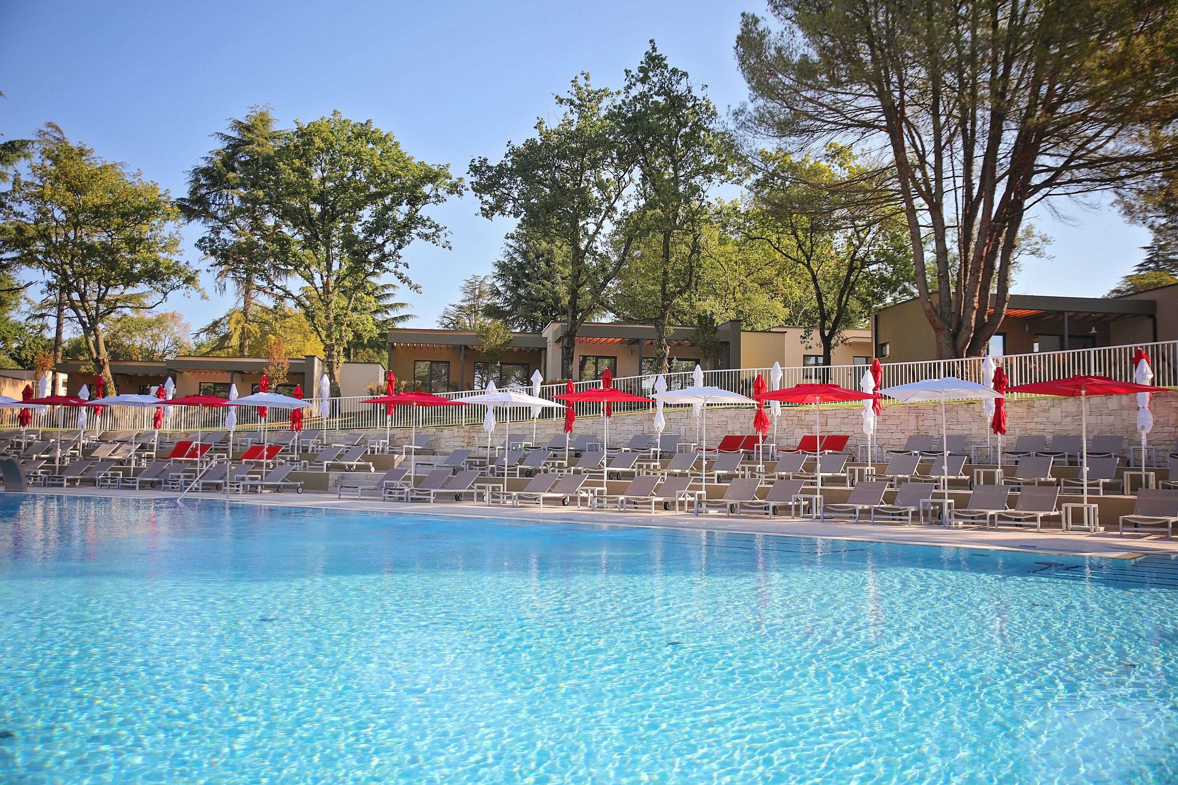 Una piscina con tumbonas y sombrillas, rodeada de árboles y edificios.