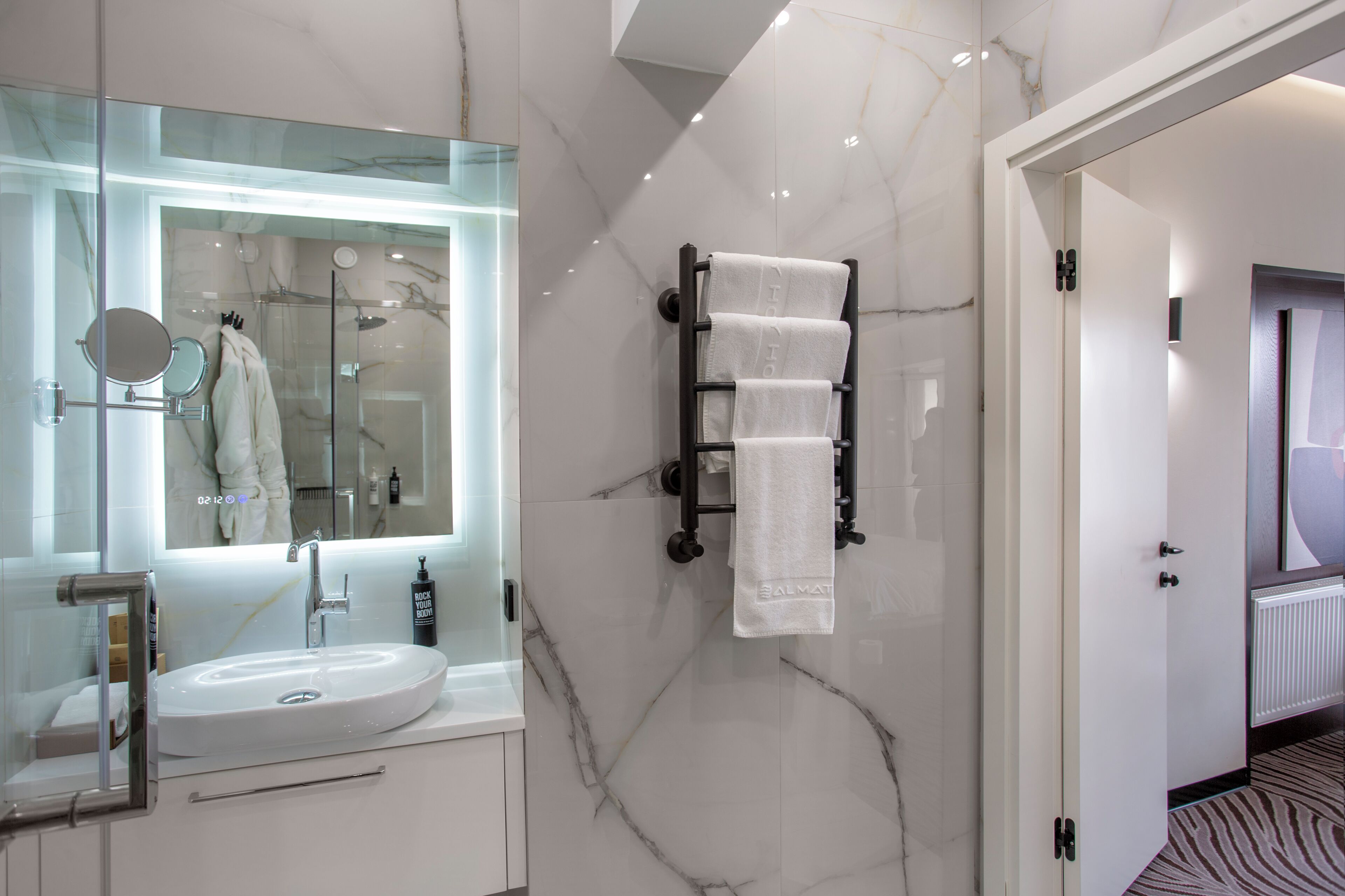A modern bathroom with a glass-enclosed shower, a white sink, and a towel rack.