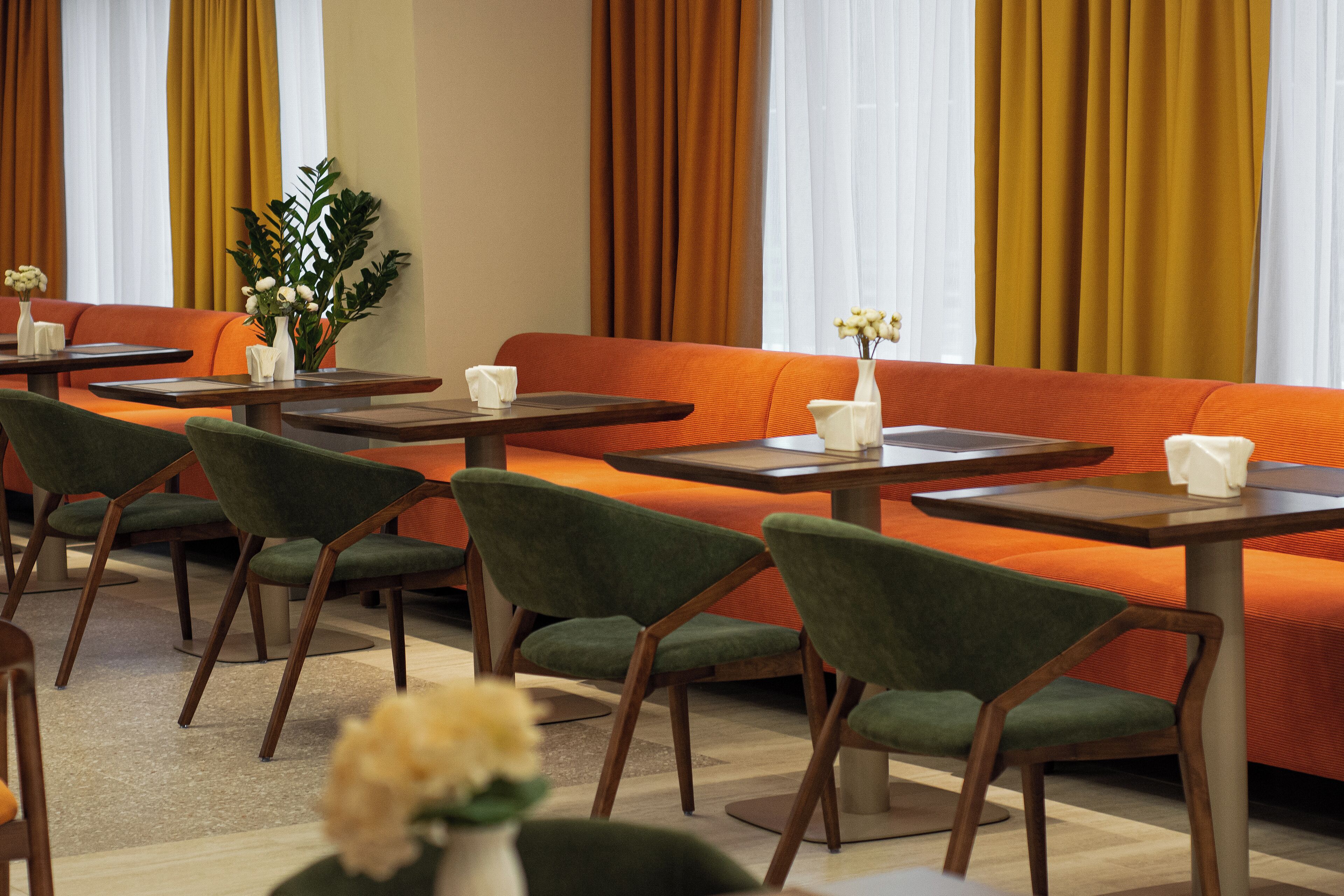Un hall moderno de hotel con asientos naranja, sillas verdes y mesas de madera.