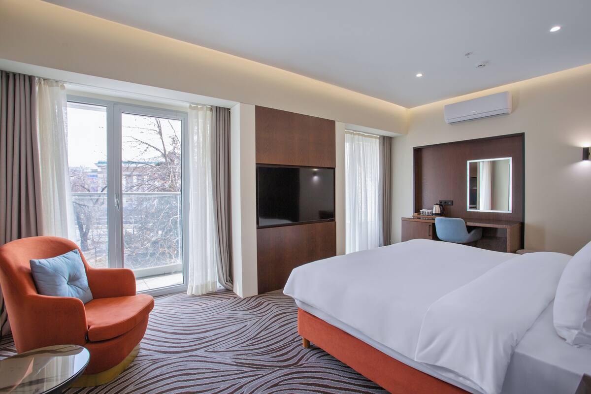 A hotel room with a bed, a TV, a desk, a chair, and a window with curtains.