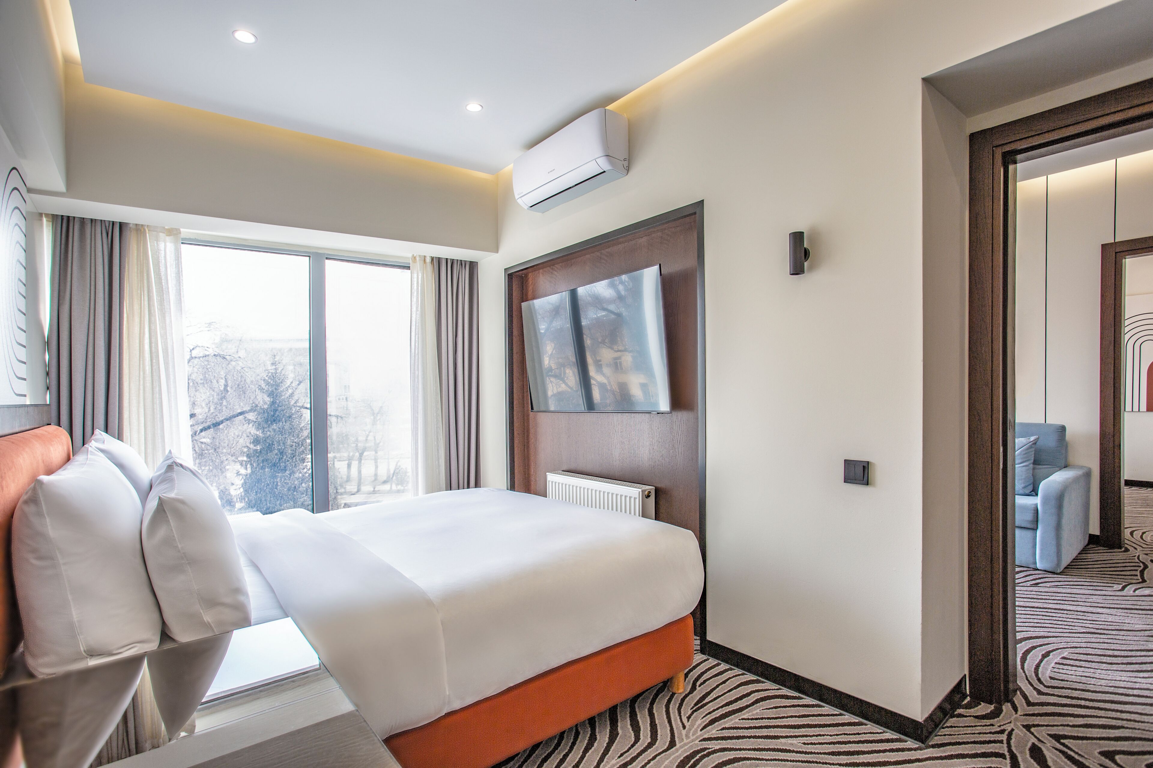 Una habitación de hotel con una cama, un televisor, una ventana y una puerta que da a otra habitación.