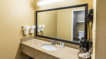 A hotel bathroom with a granite countertop sink, a large mirror, and a hairdryer mounted on the wall.