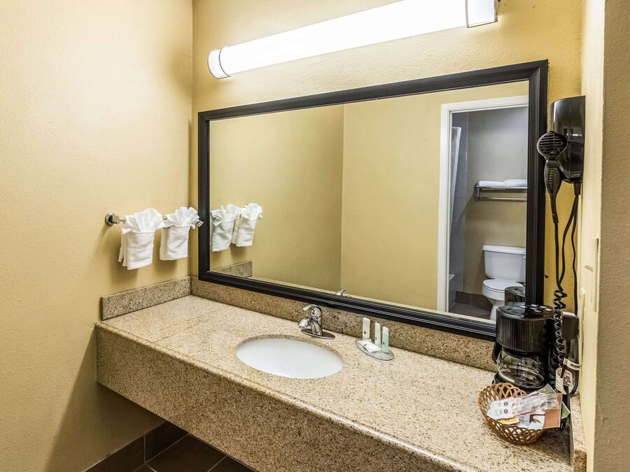 A hotel bathroom with a granite countertop sink, a large mirror, and a hairdryer mounted on the wall.