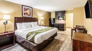 Ein Hotelzimmer mit einem großen Bett, einem Nachttisch, einem Schreibtisch, einem Sessel, einer Küchenzeile mit Kühlschrank und Mikrowelle sowie einem an der Wand befestigten Fernseher.