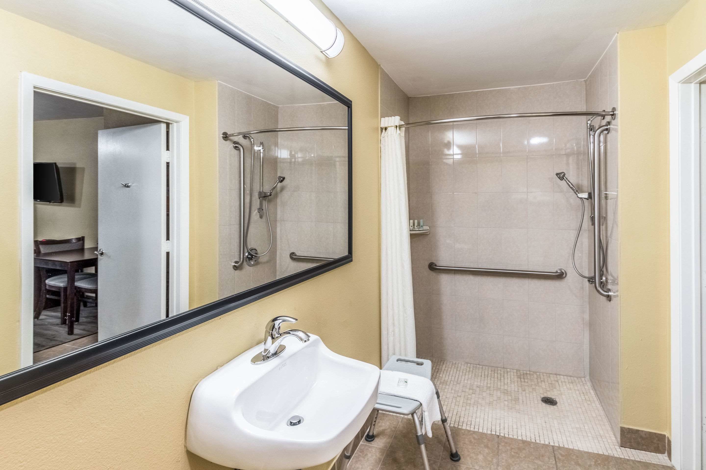 A bathroom with a sink, mirror, shower, and grab bars.