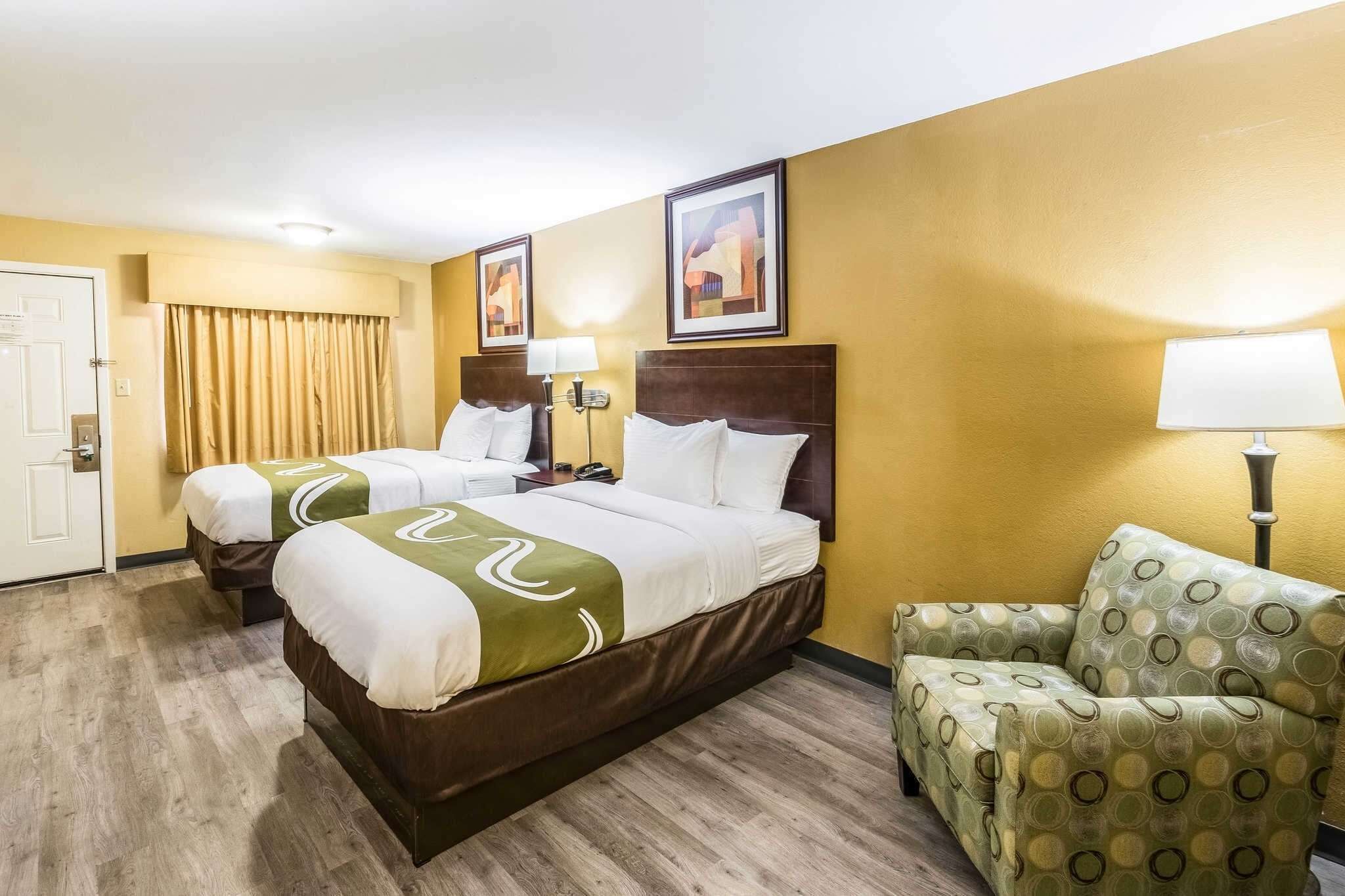 A hotel room with two beds, a sofa, and a door.