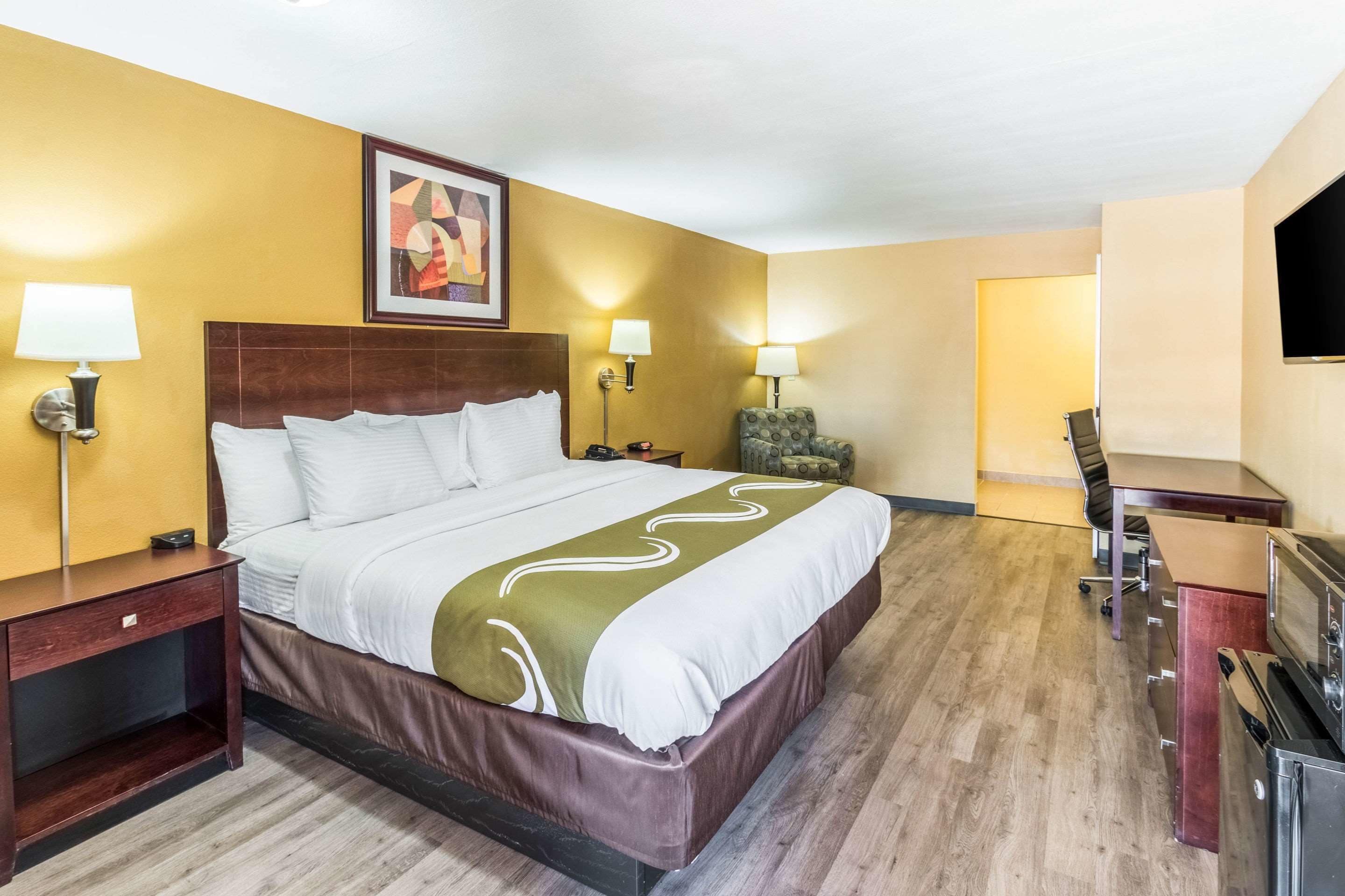 A hotel room with a large bed, bedside tables with lamps, a TV, a desk, and a chair.
