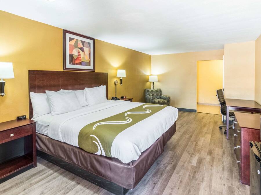 A hotel room with a large bed, bedside tables with lamps, a TV, a desk, and a chair.