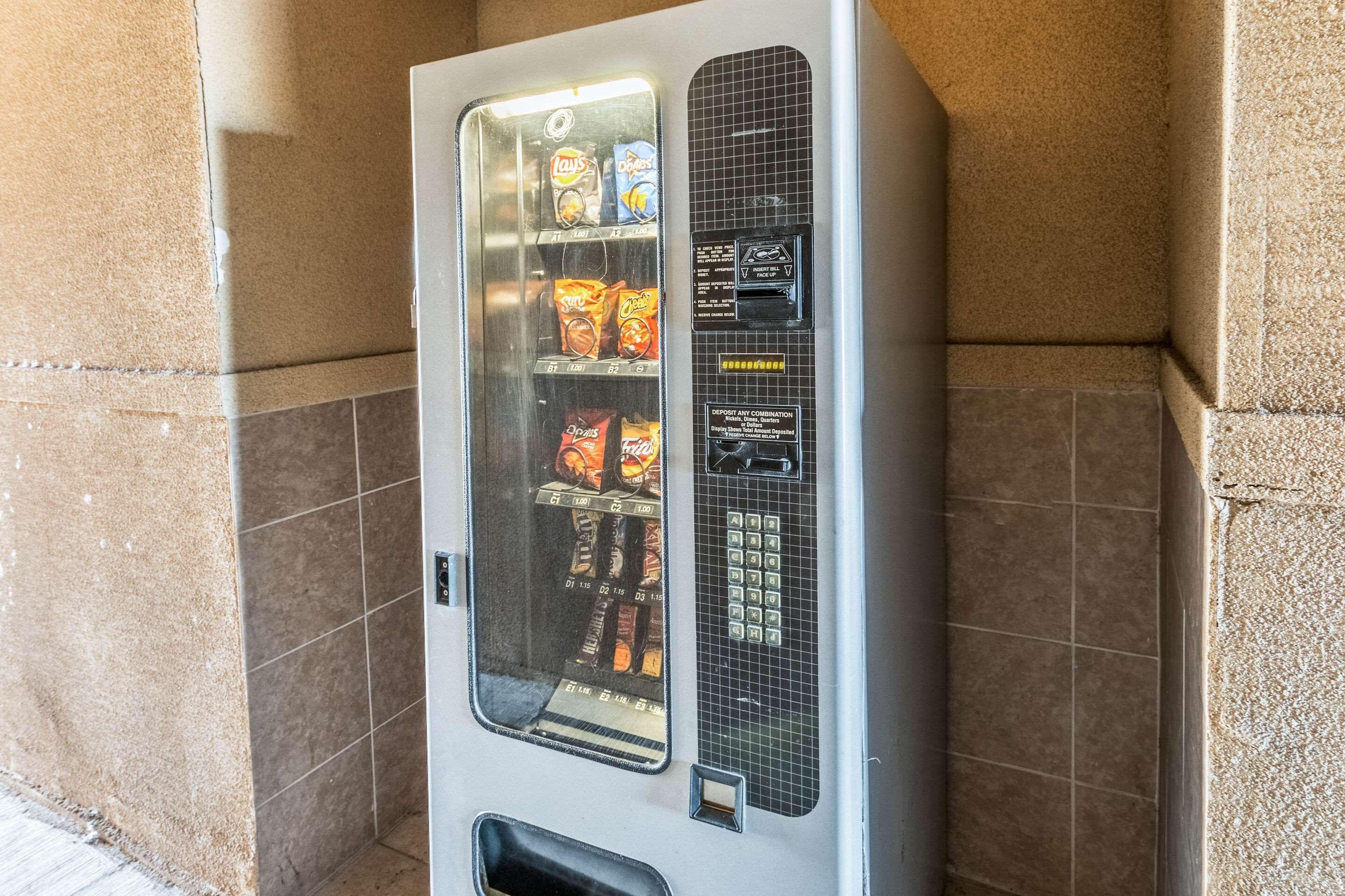 A vending machine with snacks and beverages, located in a corner with tiled walls.