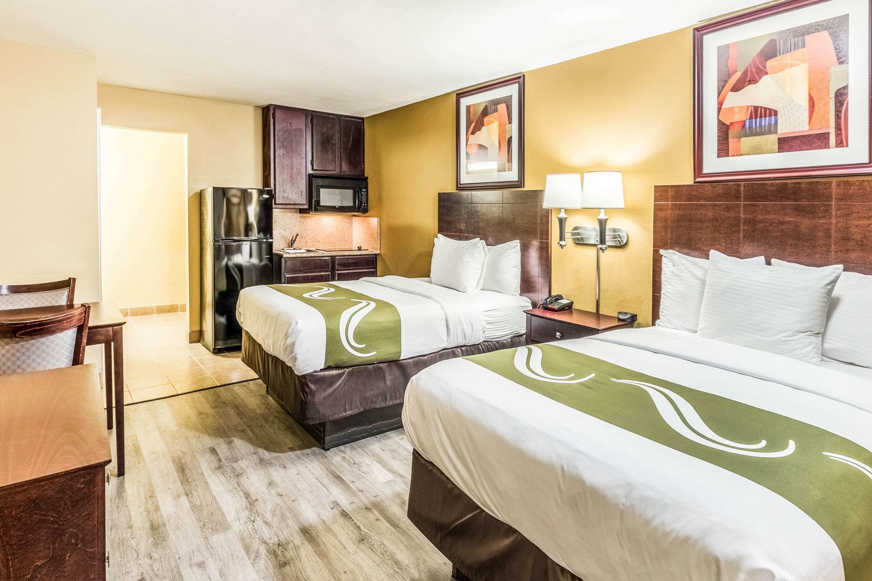 A hotel room with two beds, a desk, a chair, a microwave, and a small kitchenette.