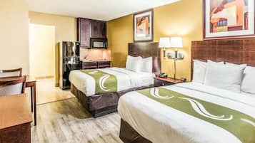 A hotel room with two beds, a desk, a chair, a microwave, and a small kitchenette.