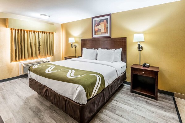 A hotel room with a large bed, two bedside lamps, a nightstand, a window with curtains, and a painting on the wall.