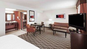 A hotel room with a bed, a desk with a chair, a sofa, a TV, and a bathroom visible through an open door. - Hampton Inn & Suites Morgan City (Morgan City)