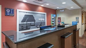 A hotel reception desk with a large poster of a beach scene and a sign that reads "enjoy." - Hampton Inn & Suites Morgan City (Morgan City)
