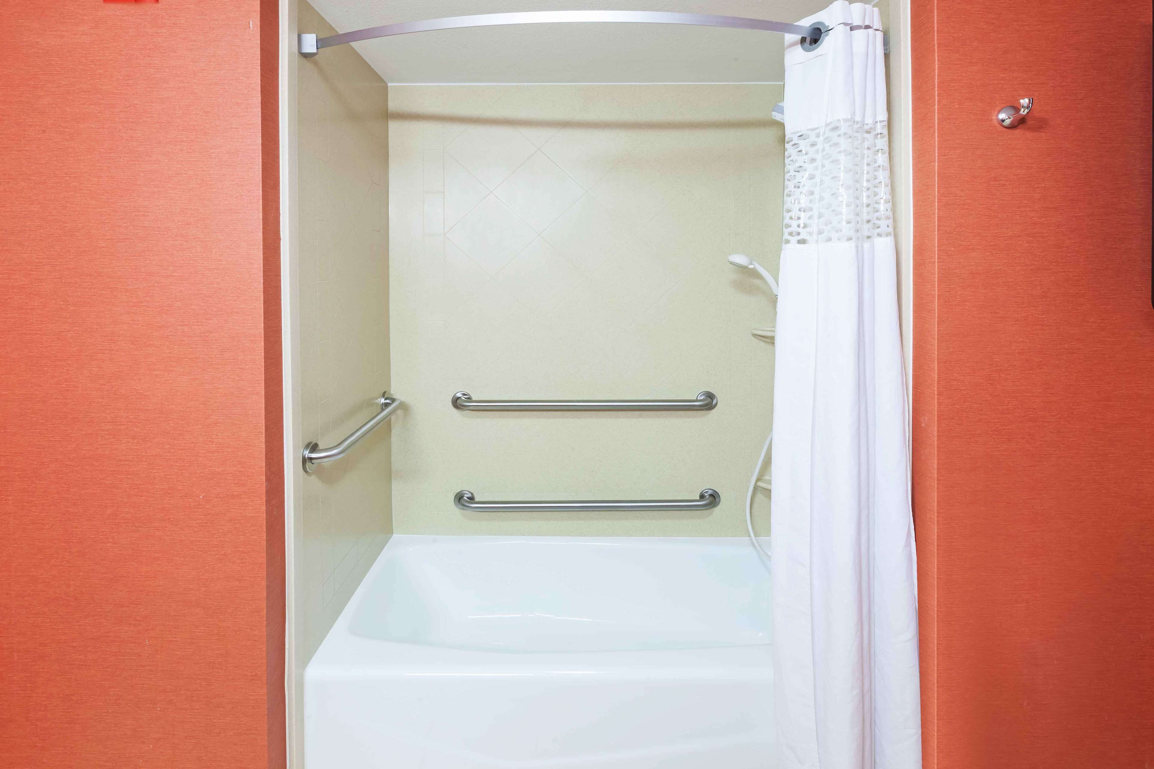 A bathroom with a bathtub, two handrails, and a shower curtain.