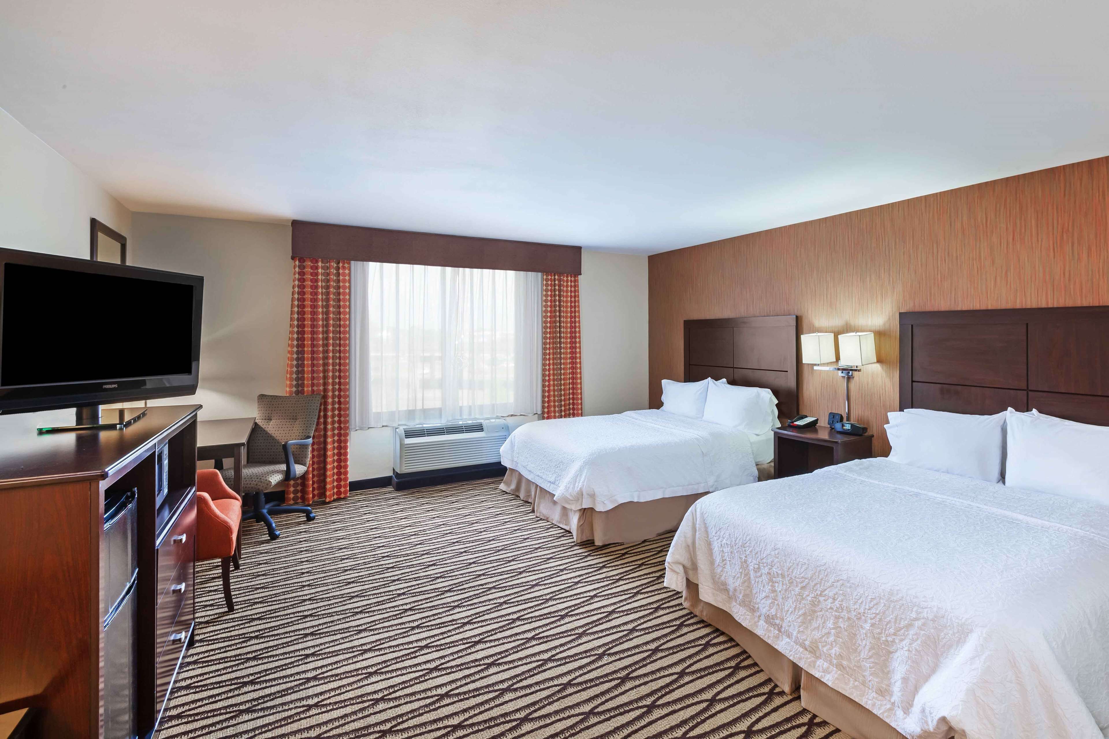 A hotel room with two beds, a TV, a desk, and a chair.