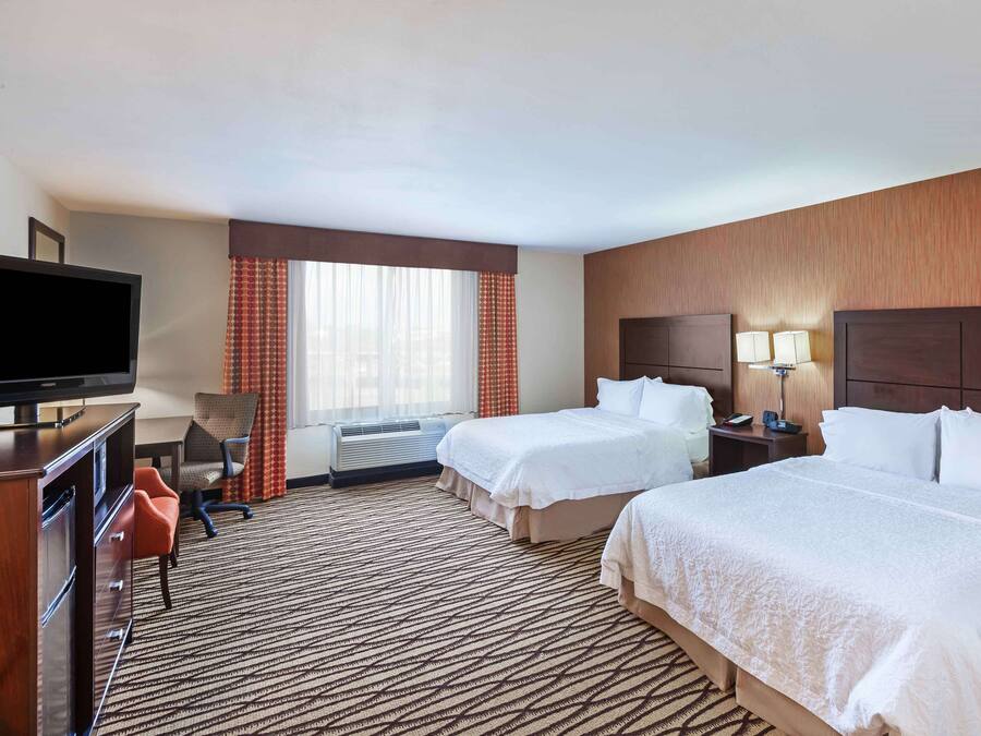 A hotel room with two beds, a TV, a desk, and a chair.