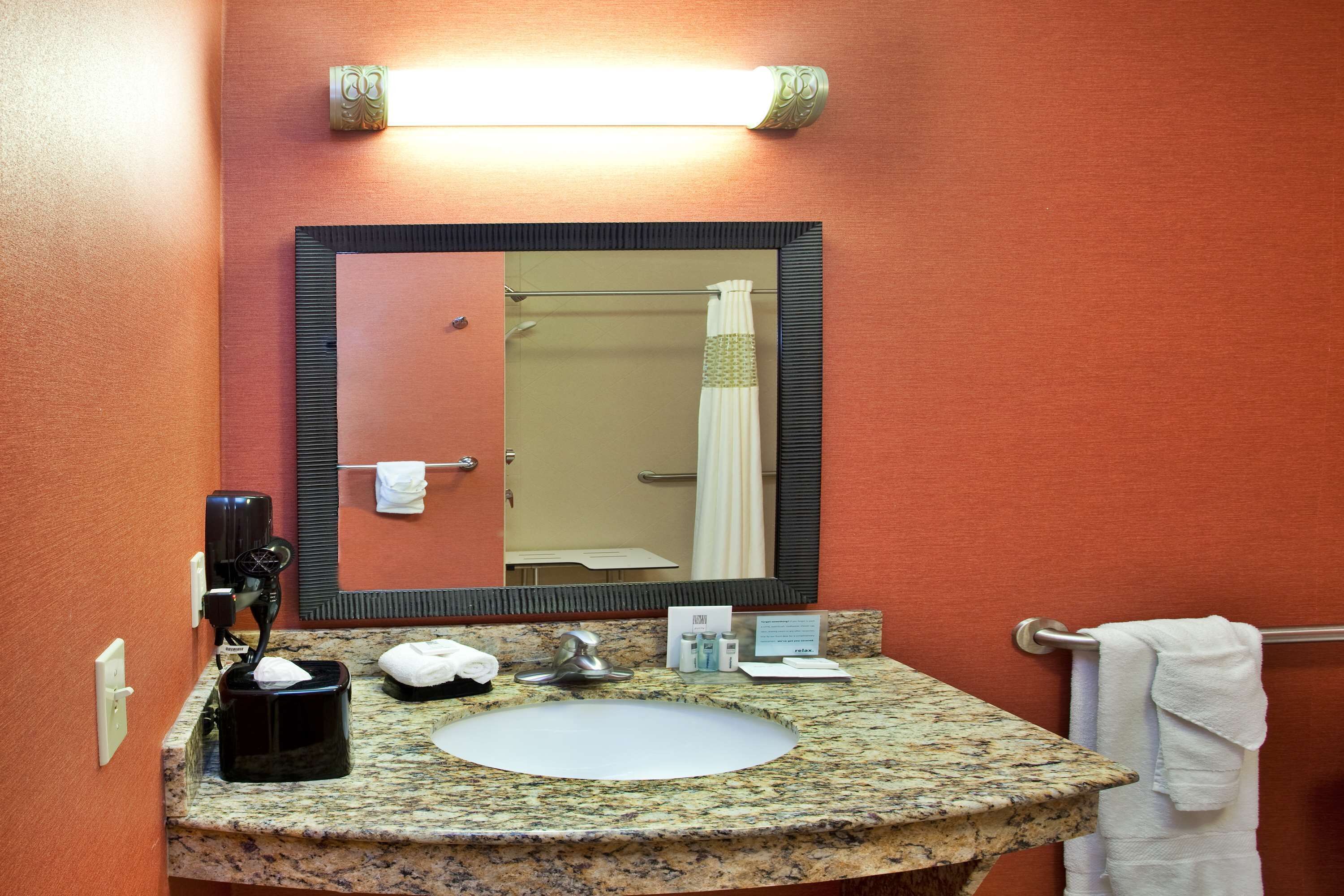 Une salle de bain avec un lavabo doté d’un plan de travail en granit, un grand miroir, un porte-serviettes et un rideau de douche.
