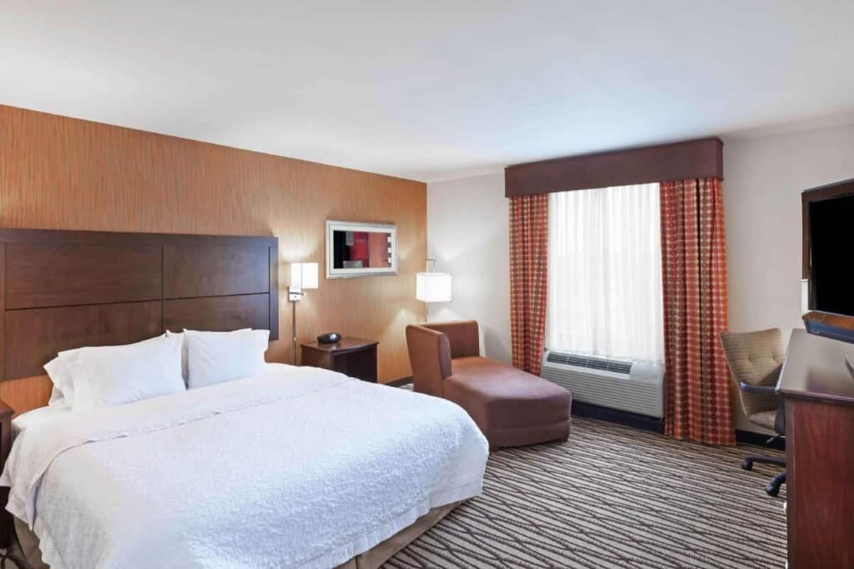 Habitación de hotel con una cama grande, un escritorio, una silla, un televisor y una ventana con cortinas.