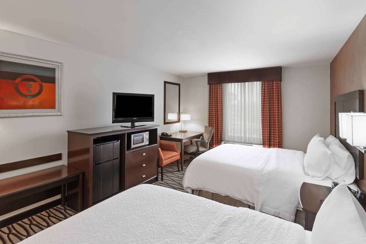 Habitación de hotel con dos camas, un escritorio con silla, televisión y un mini bar.