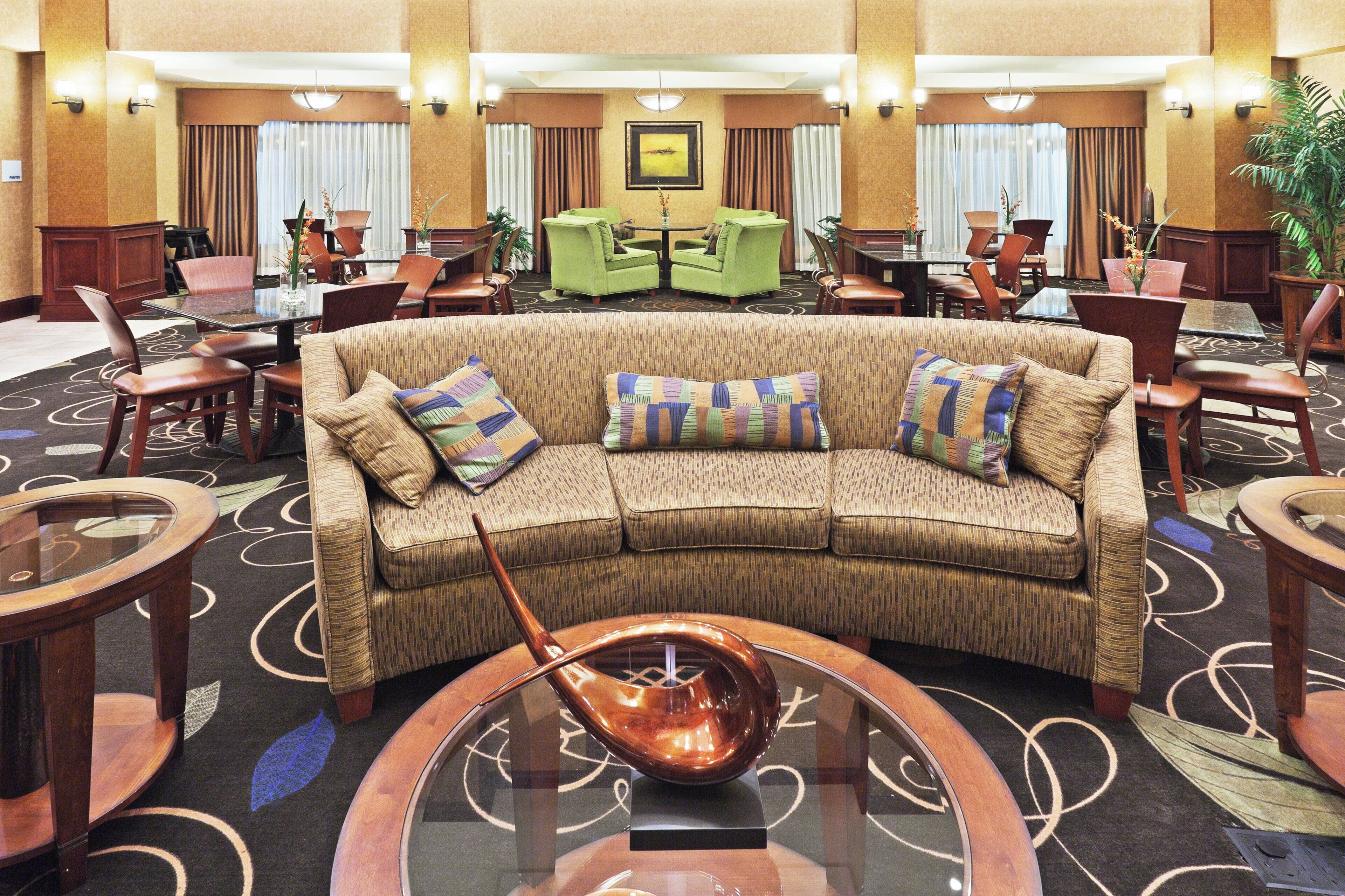 A hotel lobby with a curved sofa, multiple chairs, a dining area, and a decorative bowl on a glass table.