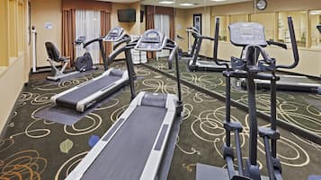 Un gimnasio hotelero con varias cintas de correr, elípticas y una bicicleta estática.