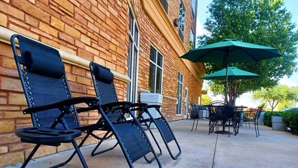 Outdoor seating with chairs and a table, a green umbrella, and a brick building in the background. - Holiday Inn Garland by IHG (Garland)