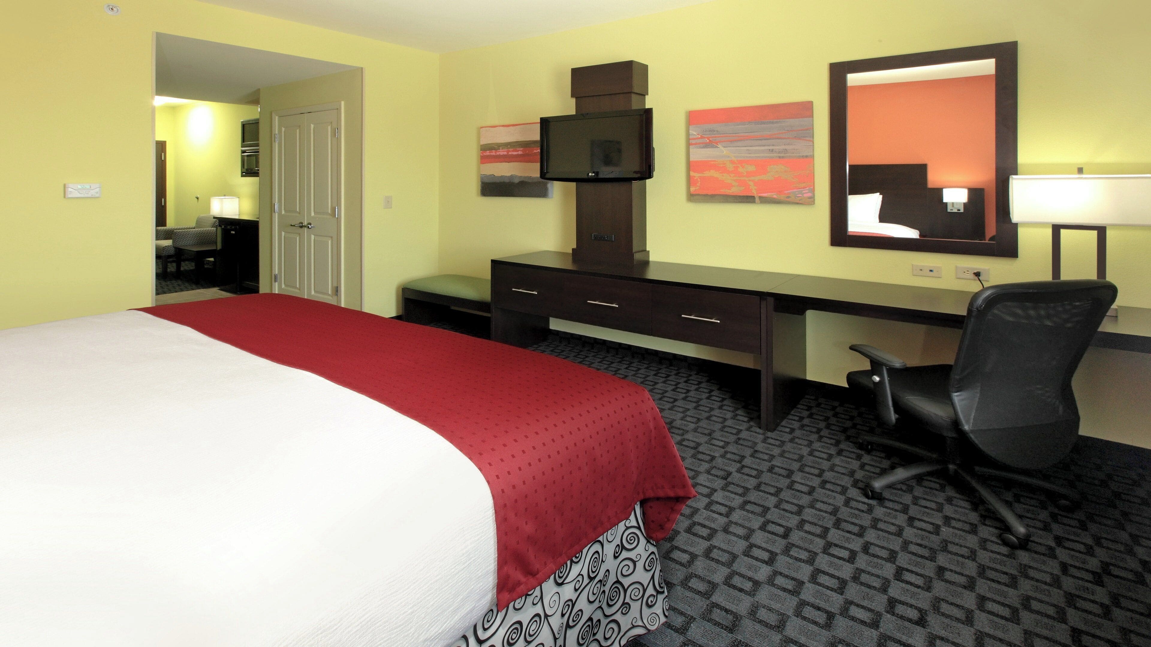 Een hotelkamer met een bed, bureau, stoel, televisie, kunstwerken en een badkamer die door een open deur zichtbaar is.