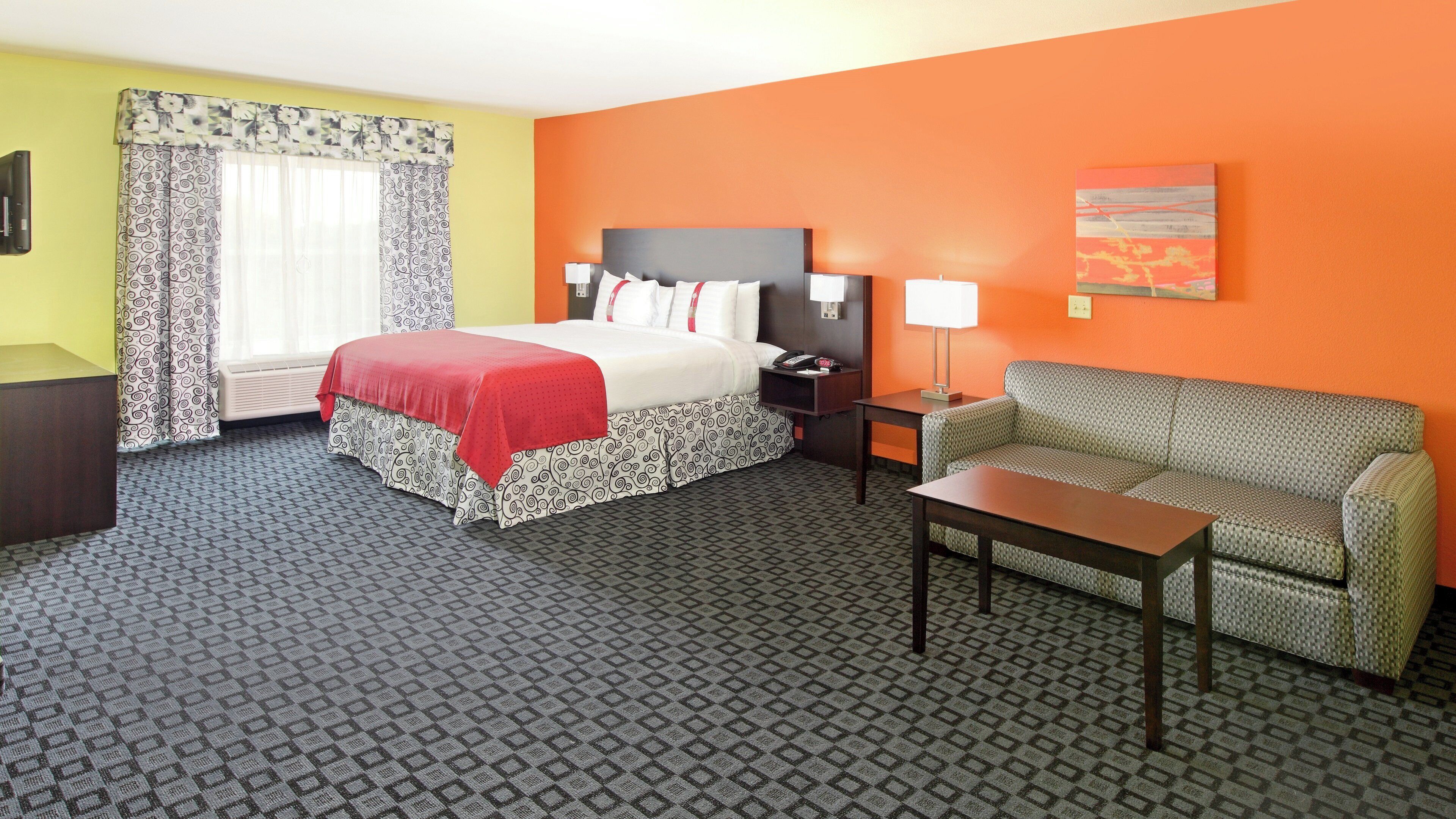 A hotel room with a bed, a sofa, a table, a lamp, and a painting on the wall.