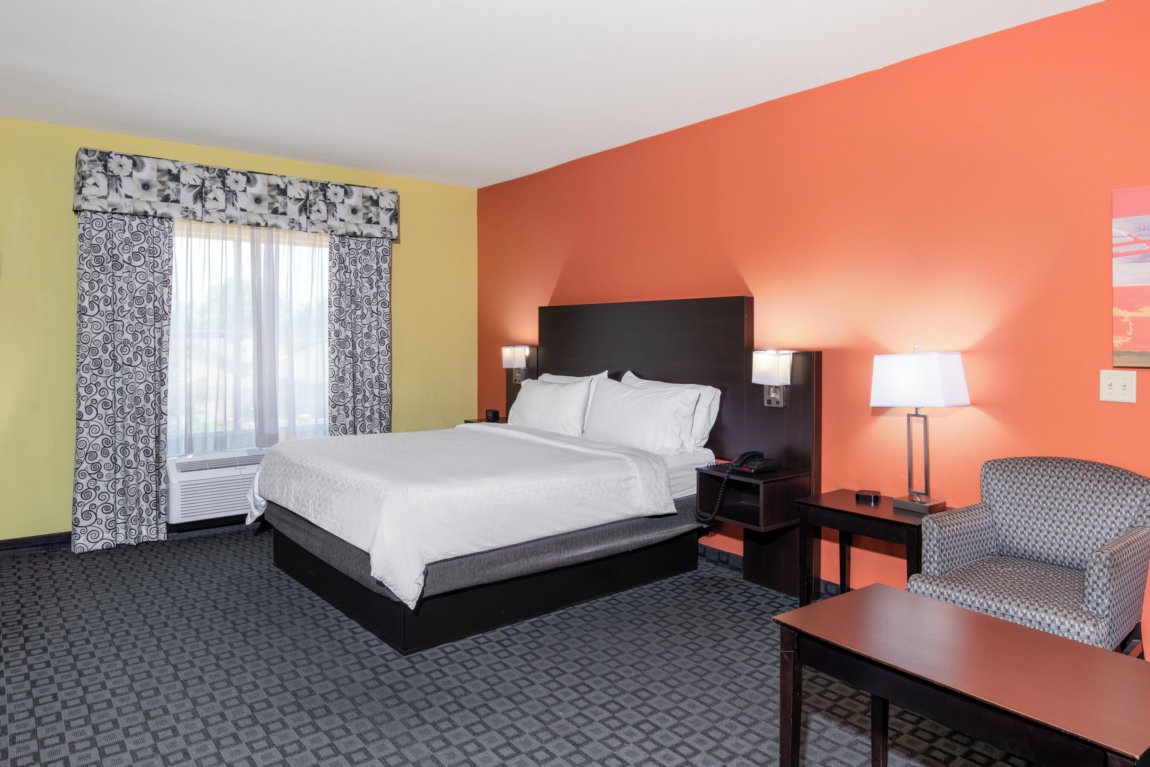 A hotel room with a bed, bedside tables, a chair, and a lamp.