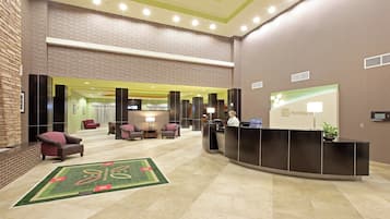 Um saguão de hotel com balcão de recepção, área de estar e um espelho grande.