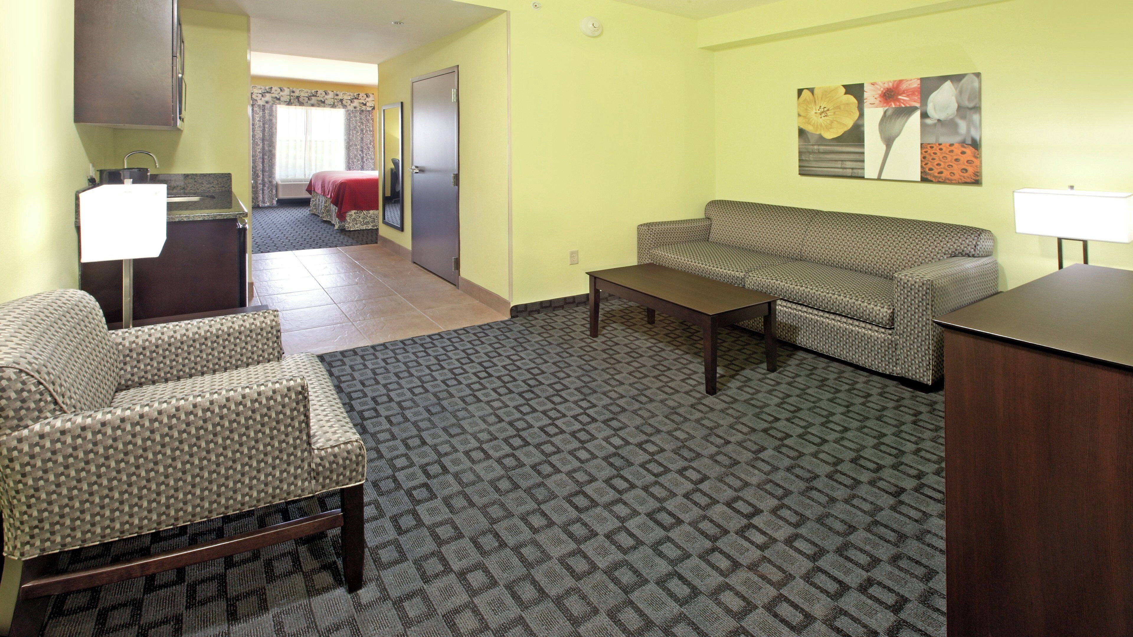 A hotel room with a sofa, armchair, and a small table. There is a door leading to a bathroom and a hallway.