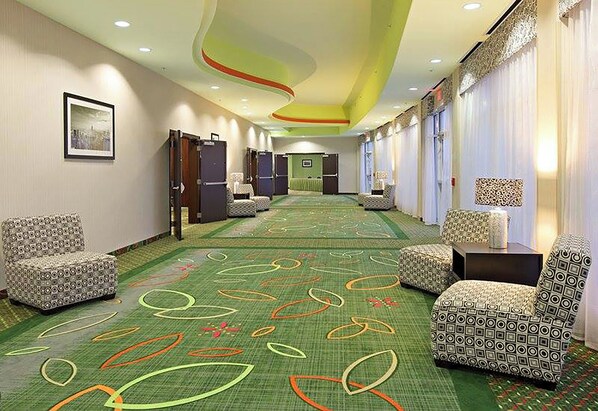 A hotel corridor with patterned carpet, seating areas, and a green wall with a framed picture. - Holiday Inn Garland by IHG (Garland)
